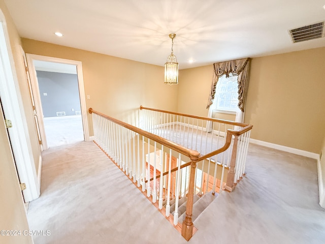 hallway featuring an inviting chandelier and light carpet