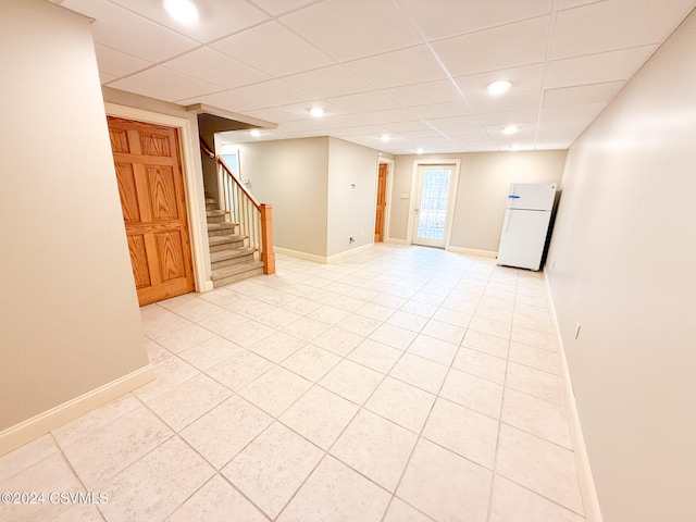 basement featuring light tile patterned floors, white fridge, and a drop ceiling