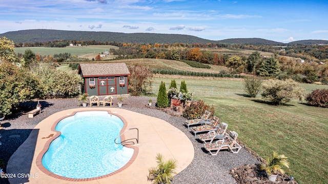 view of swimming pool featuring a patio, a mountain view, an outbuilding, and a lawn