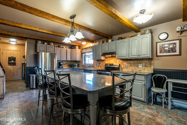 kitchen featuring tasteful backsplash, a center island, appliances with stainless steel finishes, a kitchen breakfast bar, and beamed ceiling