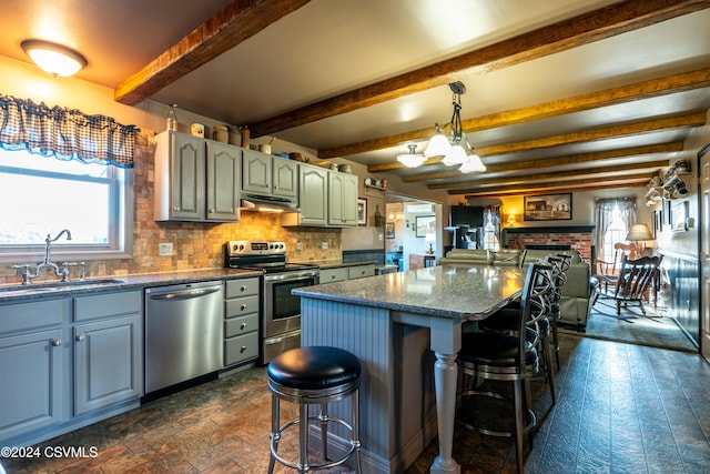 kitchen with decorative light fixtures, beamed ceiling, sink, a kitchen bar, and stainless steel appliances