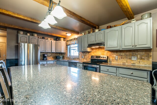 kitchen with appliances with stainless steel finishes, pendant lighting, tasteful backsplash, sink, and dark stone counters