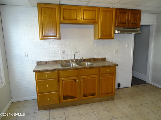 kitchen featuring a paneled ceiling, sink, brick wall, and light tile patterned floors