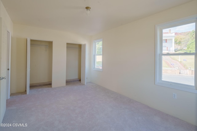 unfurnished bedroom with multiple windows, two closets, and light colored carpet