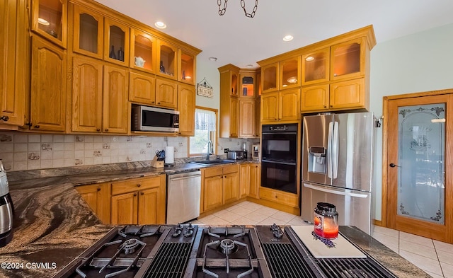 kitchen featuring stainless steel appliances, backsplash, dark stone counters, sink, and light tile patterned flooring