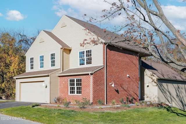 view of front of home featuring an attached garage, aphalt driveway, a front lawn, and brick siding