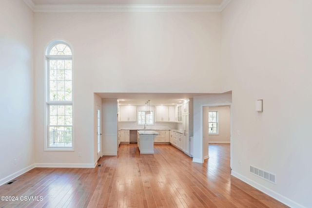 unfurnished living room with light hardwood / wood-style floors, crown molding, and a towering ceiling