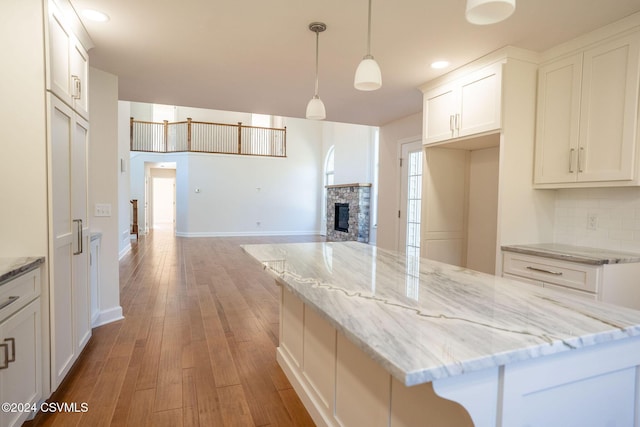 kitchen with light stone countertops, a fireplace, light wood-type flooring, white cabinets, and tasteful backsplash