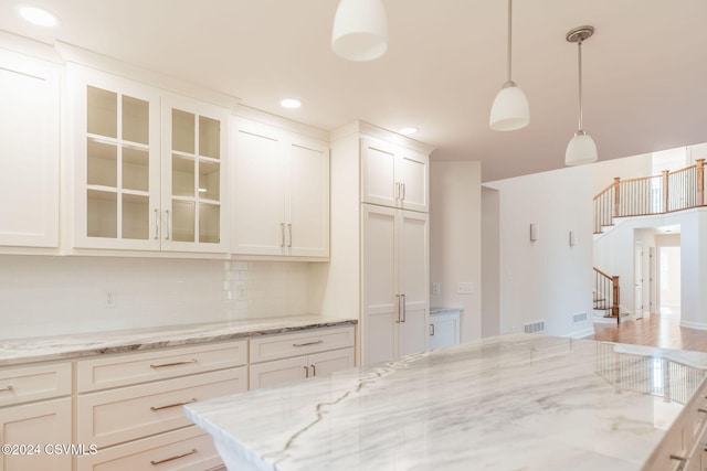 kitchen with wood-type flooring, backsplash, pendant lighting, white cabinets, and light stone counters