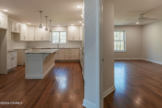 kitchen with dark wood-style flooring, a kitchen island, ceiling fan, a sink, and backsplash