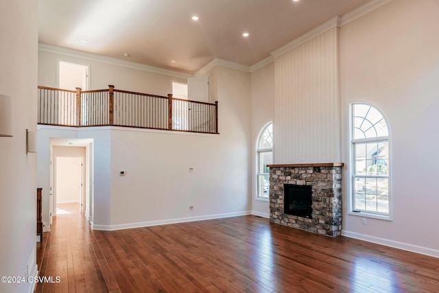 unfurnished living room with crown molding, hardwood / wood-style floors, a stone fireplace, baseboards, and a high ceiling