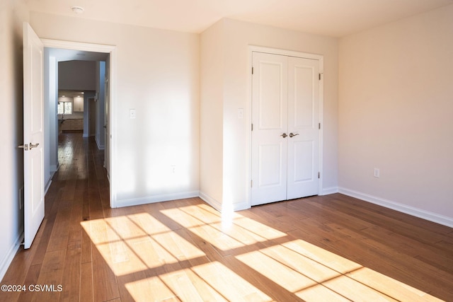 unfurnished bedroom with wood-type flooring, baseboards, and a closet