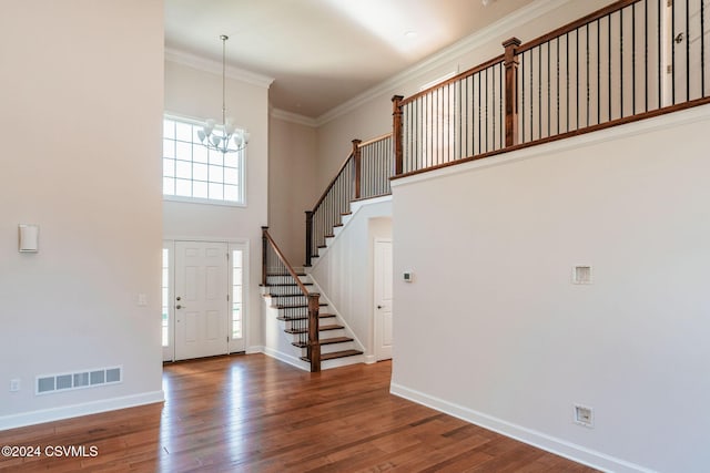 entryway with a towering ceiling, visible vents, wood finished floors, an inviting chandelier, and stairs