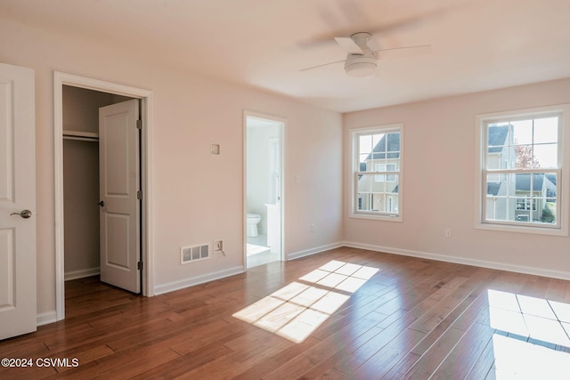 unfurnished bedroom featuring connected bathroom, a walk in closet, baseboards, wood finished floors, and visible vents