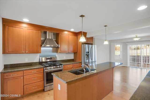 kitchen featuring light hardwood / wood-style floors, stainless steel appliances, sink, an island with sink, and wall chimney range hood