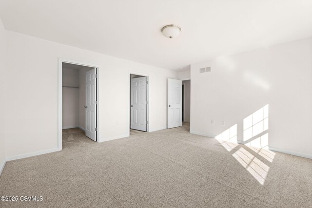 unfurnished bedroom featuring a spacious closet, light carpet, and a closet