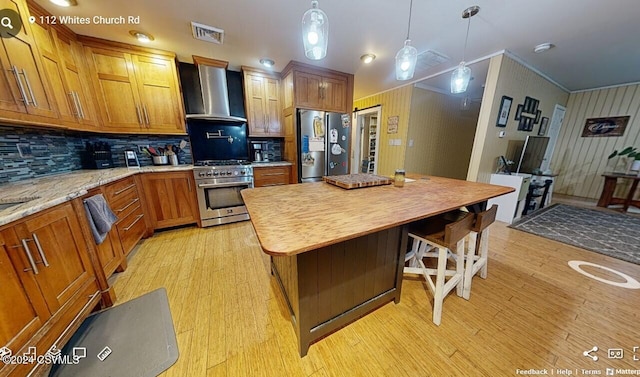 kitchen with decorative backsplash, stainless steel appliances, light hardwood / wood-style floors, wall chimney exhaust hood, and decorative light fixtures