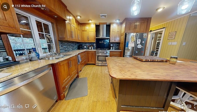 kitchen with wall chimney exhaust hood, pendant lighting, stainless steel appliances, and backsplash