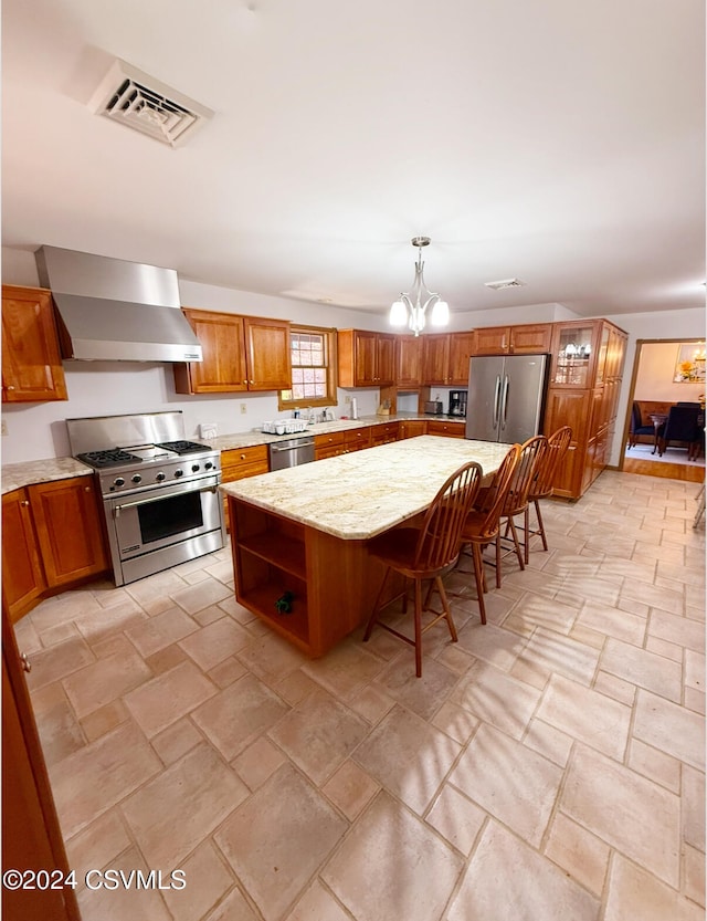 kitchen featuring wall chimney exhaust hood, a kitchen island, a breakfast bar, pendant lighting, and appliances with stainless steel finishes