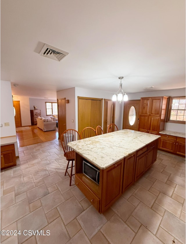 kitchen featuring a kitchen bar, stainless steel microwave, a chandelier, a kitchen island, and pendant lighting