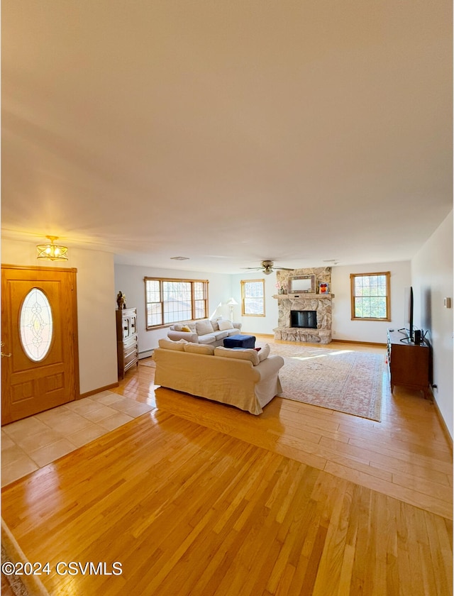 unfurnished living room with ceiling fan, light hardwood / wood-style floors, and a stone fireplace