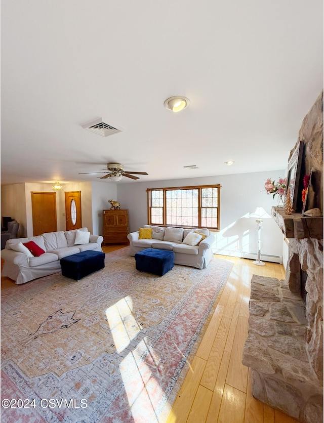 living room with a stone fireplace, ceiling fan, and light hardwood / wood-style flooring