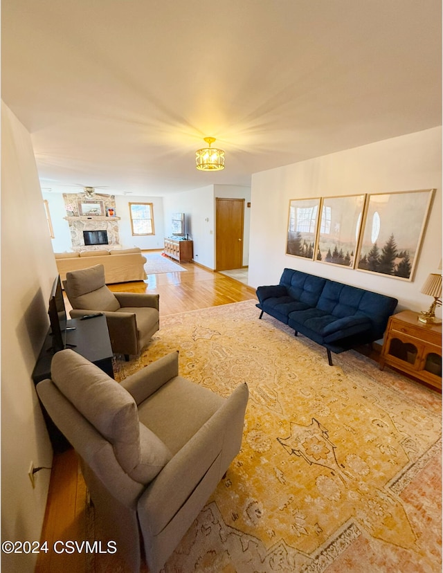 living room with a stone fireplace, light wood-type flooring, and a notable chandelier