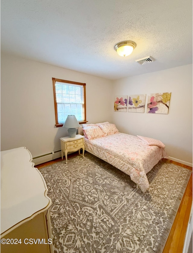 bedroom featuring hardwood / wood-style floors, a baseboard radiator, and a textured ceiling