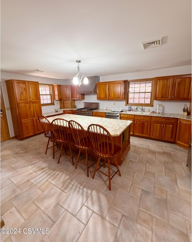 kitchen with appliances with stainless steel finishes, a kitchen bar, decorative light fixtures, a center island, and wall chimney range hood