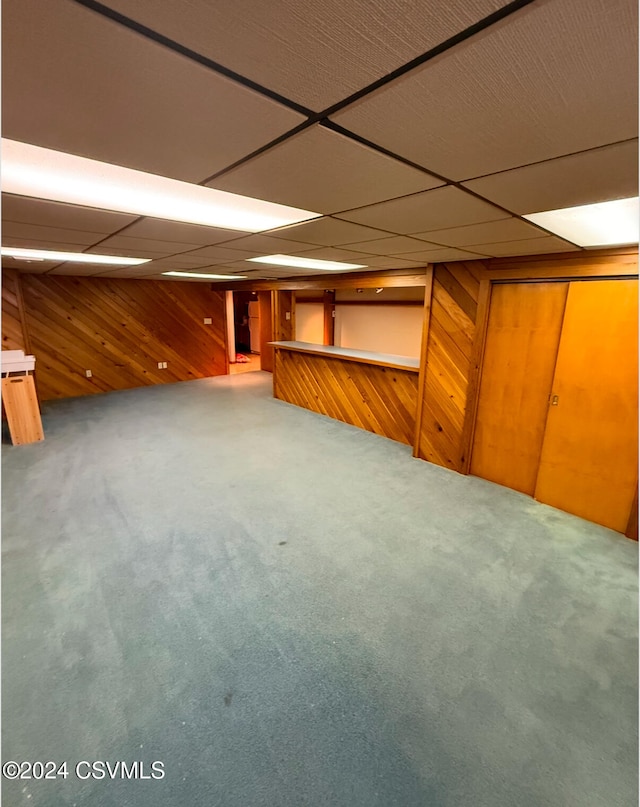 basement featuring wooden walls, carpet floors, and a paneled ceiling