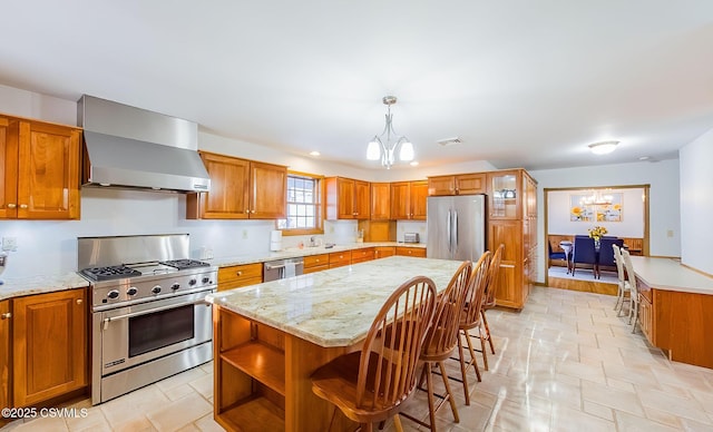 kitchen with wall chimney exhaust hood, decorative light fixtures, a center island, an inviting chandelier, and stainless steel appliances