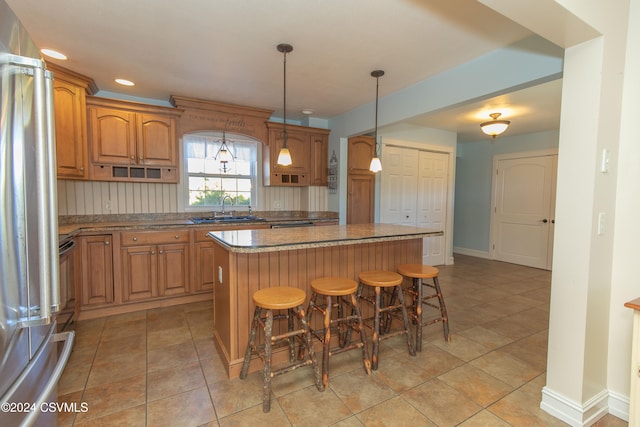 kitchen featuring sink, a breakfast bar area, a center island, stainless steel fridge, and pendant lighting