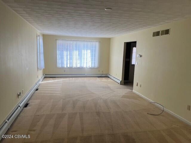 carpeted spare room featuring a baseboard heating unit