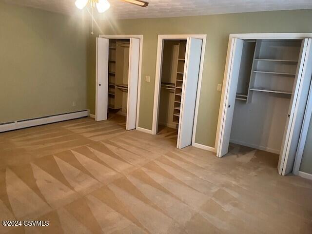 unfurnished bedroom featuring ceiling fan, a textured ceiling, light carpet, and two closets