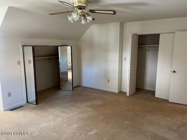 unfurnished bedroom featuring light carpet, lofted ceiling, ceiling fan, and two closets