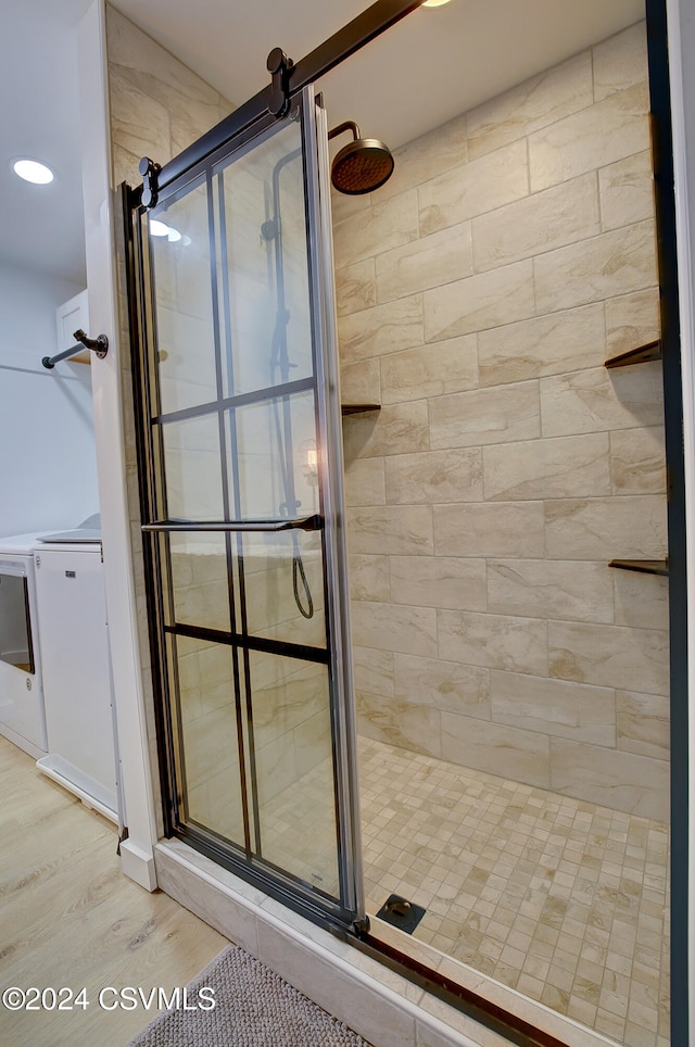 bathroom with hardwood / wood-style flooring, separate washer and dryer, and a shower with door