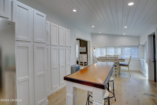 kitchen with white cabinets, stainless steel fridge, light hardwood / wood-style flooring, and lofted ceiling