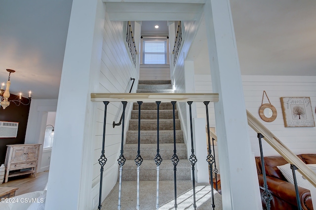 stairs featuring hardwood / wood-style floors, a wall unit AC, wooden walls, and an inviting chandelier