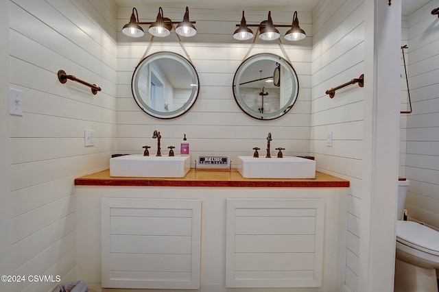 bathroom featuring toilet, wood walls, and vanity