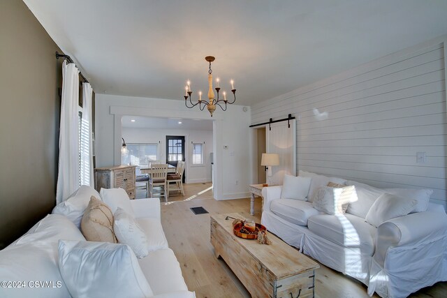 living room featuring light hardwood / wood-style flooring, a notable chandelier, a barn door, and wooden walls