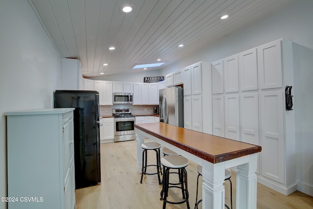 kitchen with white cabinets, a kitchen breakfast bar, appliances with stainless steel finishes, and light wood-type flooring