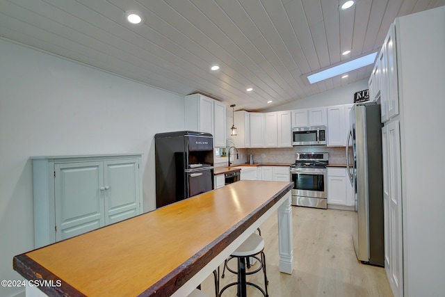 kitchen featuring stainless steel appliances, light hardwood / wood-style floors, vaulted ceiling, white cabinets, and decorative backsplash