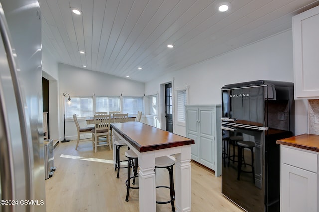 kitchen featuring lofted ceiling, wood counters, white cabinetry, light hardwood / wood-style flooring, and stainless steel fridge