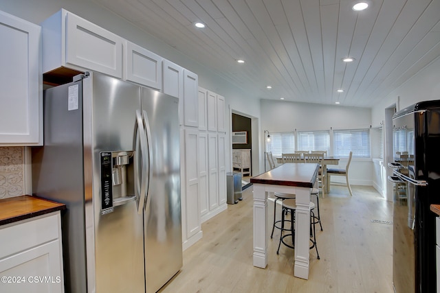 kitchen featuring white cabinets, lofted ceiling, stainless steel fridge, and wood counters