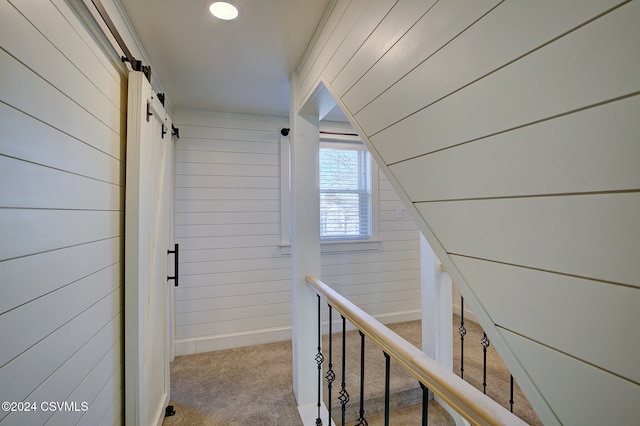 hallway featuring light colored carpet, wooden walls, and a barn door