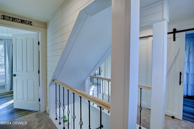 corridor featuring wood walls, a barn door, ornamental molding, and carpet floors