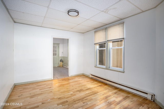 spare room with baseboard heating, a drop ceiling, and wood-type flooring