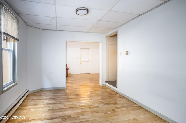 spare room with a drop ceiling, a baseboard radiator, and light wood-type flooring