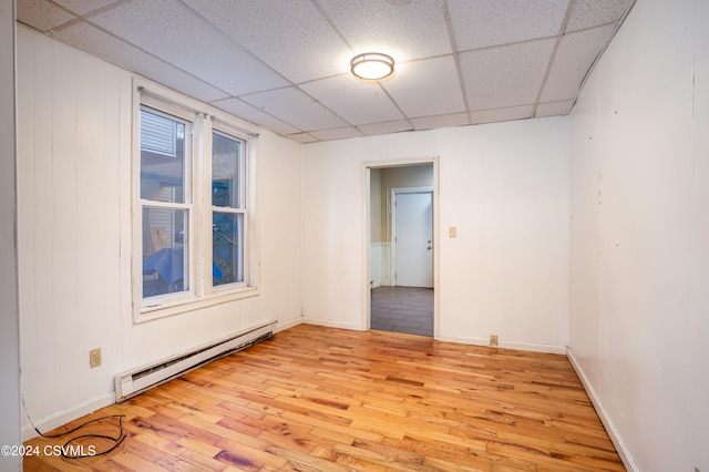 empty room featuring light hardwood / wood-style flooring, baseboard heating, and a paneled ceiling