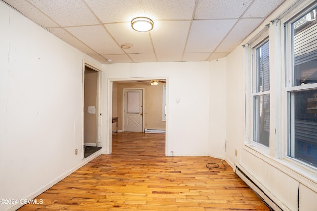 spare room featuring a drop ceiling, a baseboard radiator, and light hardwood / wood-style floors